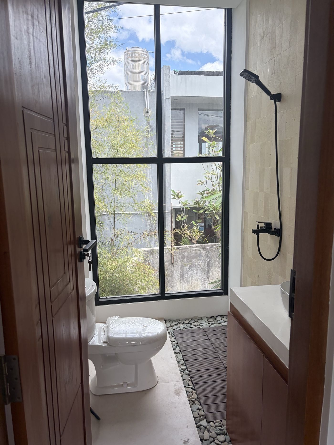 On site, Villa 1: bathroom with full-height black-framed window, stone floor and timber door
