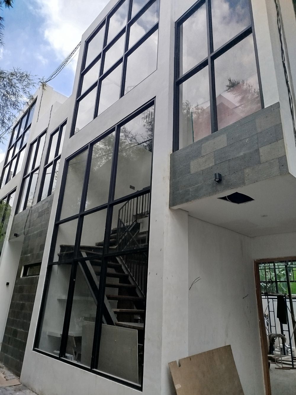 Villa 2 build progress: facade with black-framed glazing and stone cladding, stair visible inside