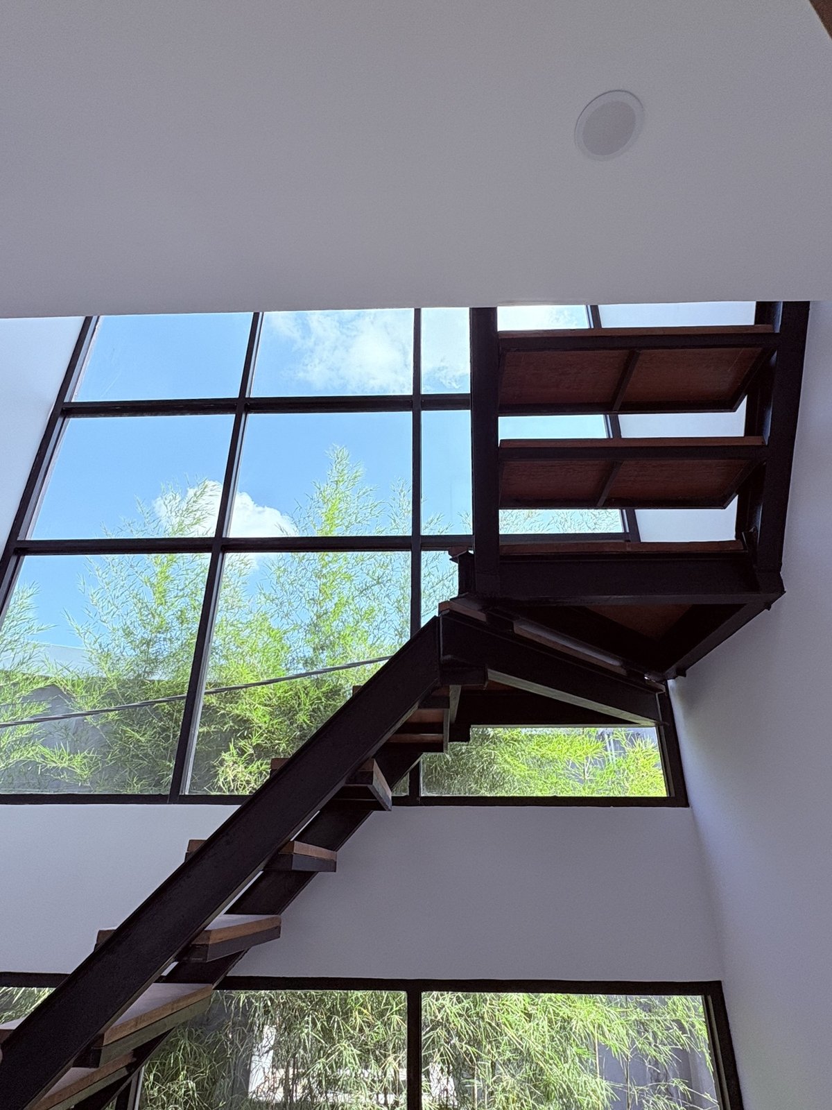 On site: floating steel-and-timber staircase against full-height black-framed glazing and open sky